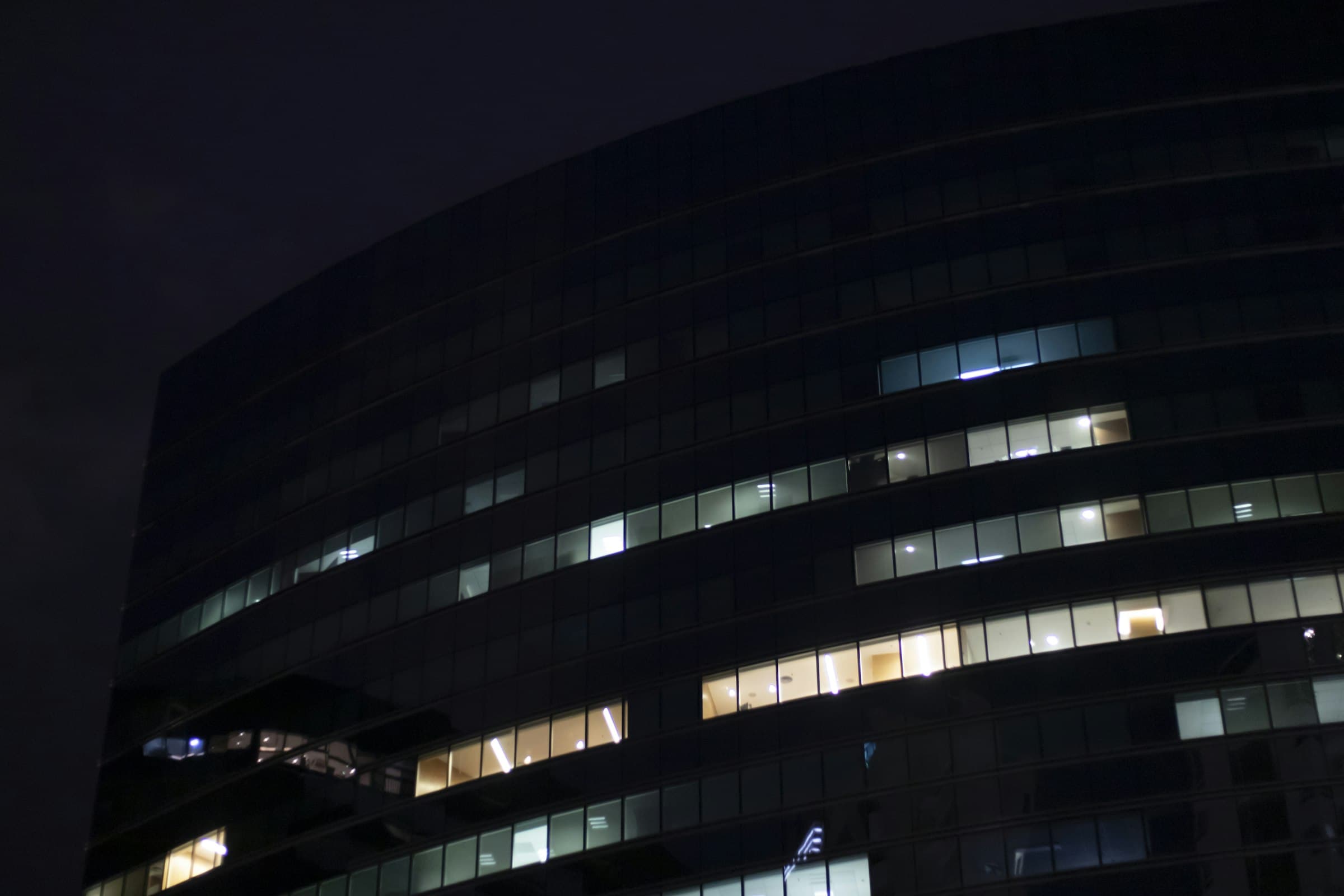 Curved office tower at night with scattered lit windows