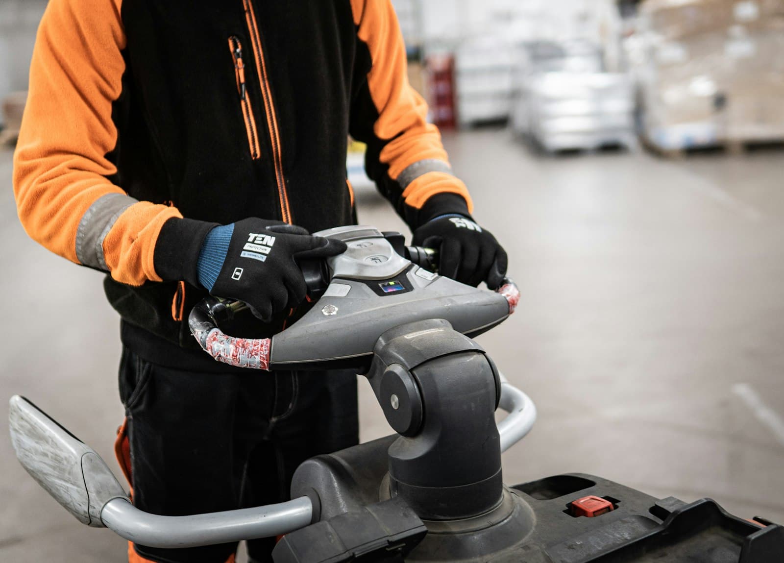 A warehouse worker in gloves handling equipment on the floor
